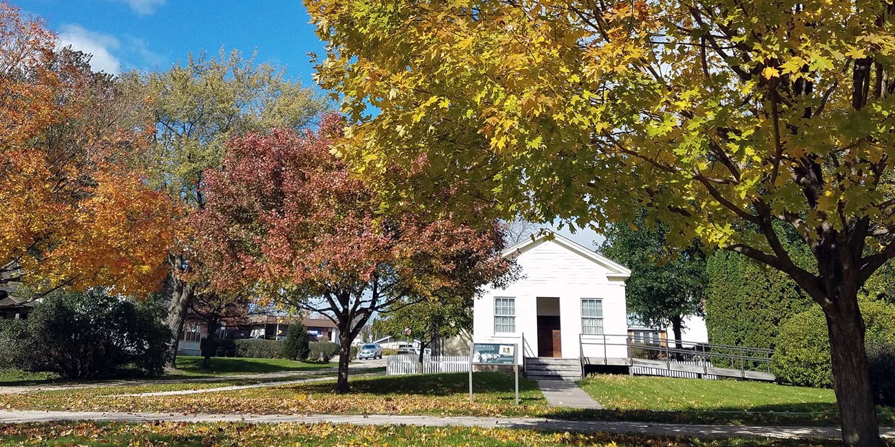 Trees in brilliant autumn foliage frame an old white schoolhouse.