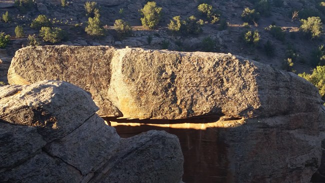 two beams of light meeting across a boulder face, spiral petroglyphs barely visible