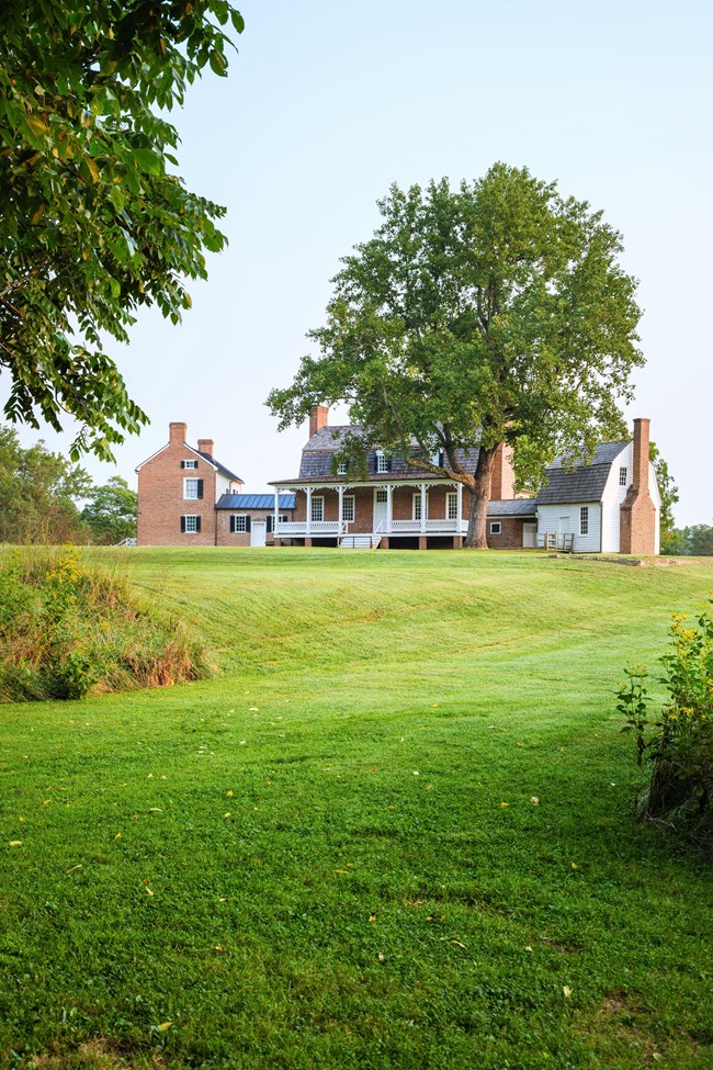 Thomas Stone House at THST A red bricked house sits at the top of a green hill, with trees on either side