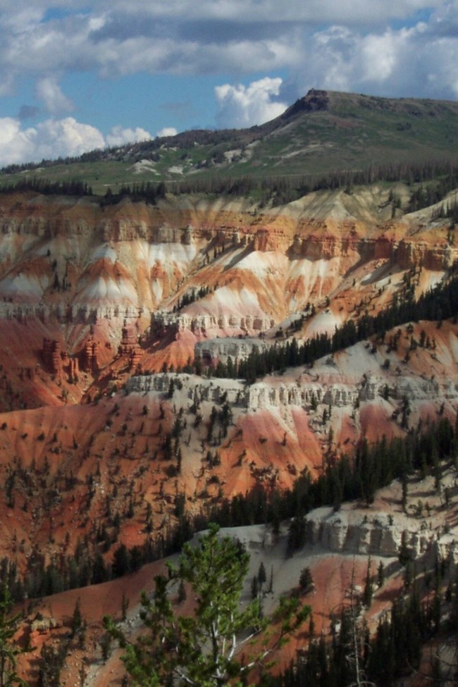Topped with snow and framed by red cliffs, Brian Head Peak is the high point of the Markagunt Plateau. Brian Head Peak behind Cedar Breaks’ colorful cliffs, with lingering snow and conifer forest.