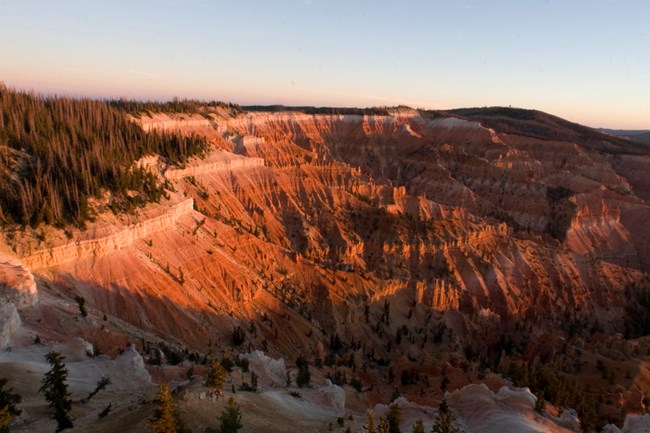 Carved into the Claron Formation, the Cedar Breaks Amphitheater showcases striking color and erosion. Cedar Breaks Amphitheater lit by sunset, revealing deep orange and red geologic formations.