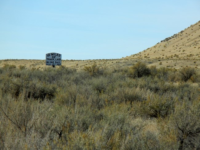 Sagebrush landscape with sign saying "Ten miles of track laid in one day, April 28, 1869."