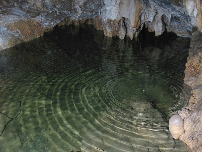 Still and pristine, Hansen Lake reflects the underground beauty of Timpanogos Cave. Clear water rippling in a cave pool beneath stalactites.