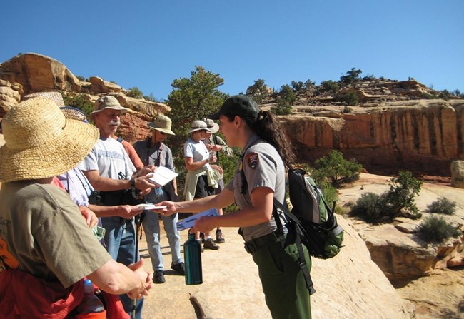 Guided hikes at Capitol Reef foster visitor awareness about protecting sensitive desert habitats. Ranger handing out materials to visitors on a guided hike in a rocky desert setting.