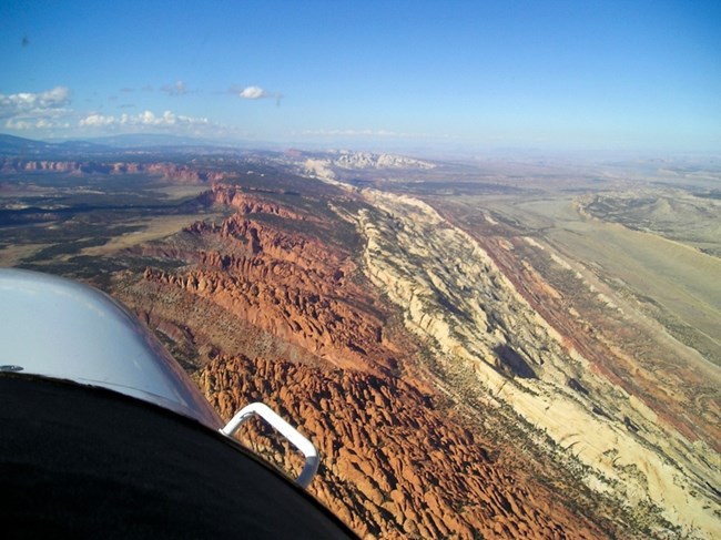 The Waterpocket Fold, a nearly 100-mile-long monocline, defines Capitol Reef’s dramatic geologic landscape. Aerial view of the Waterpocket Fold with tilted rock layers and narrow valleys looking north.