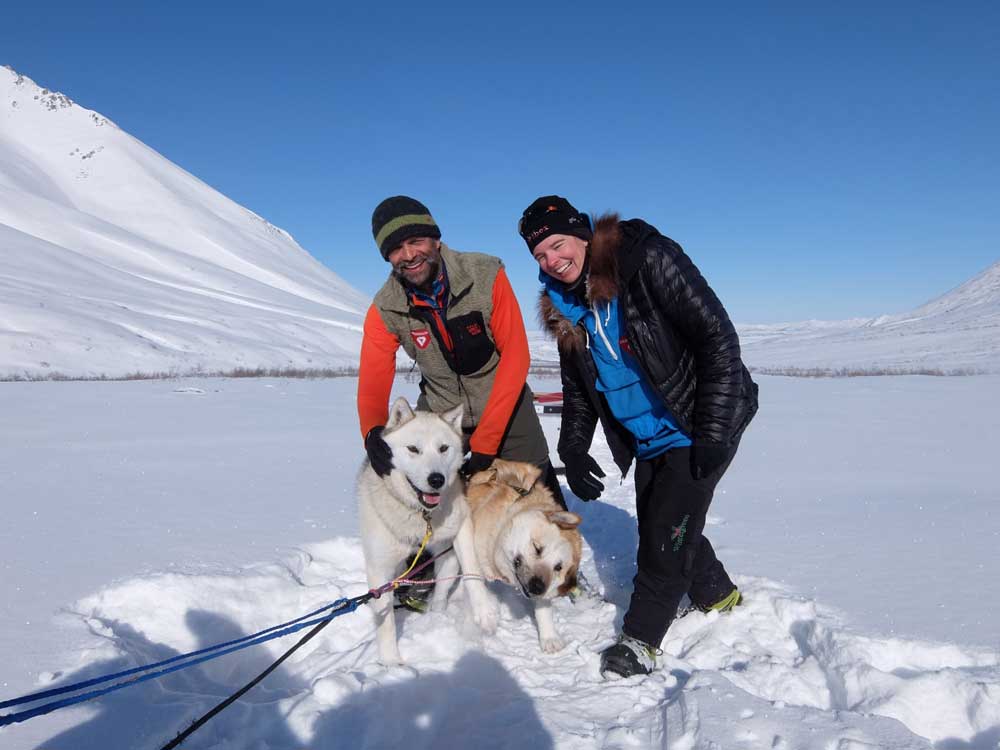 man and woman petting sled dogs in a snowy landscape