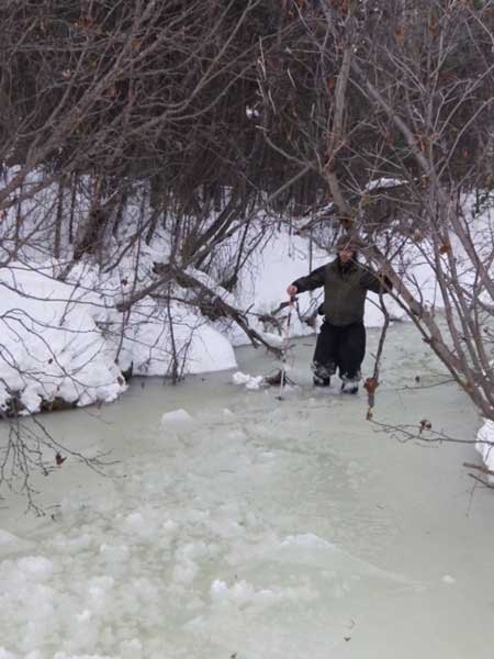 a man wading through knee deep slushy water in a snowy forest