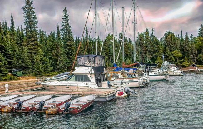 Four small, red fishing boats, a large powerboat, and multiple sailboats docked in a marina.