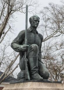 A color photo of a statue of Jim Bowie on one knee holding a long muzzled gun at his side, pointed at the sky.