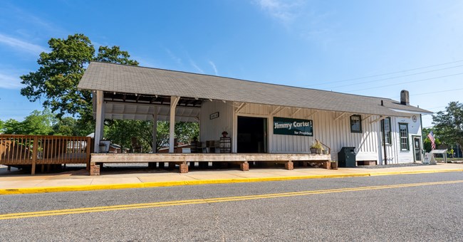 A small building next to train tracks. the building has a green sign that reads, "Jimmy Carter! For President".