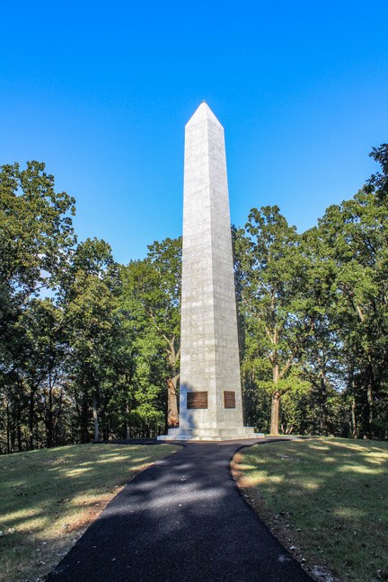 A obelisk rises above the trees as the sun sets.