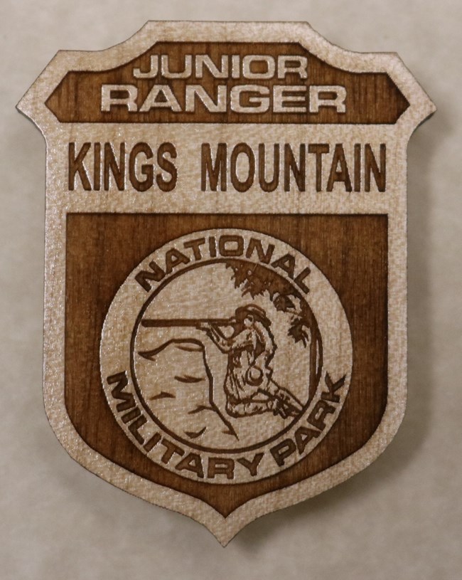 A wooden badge that has Kings Mountain on it