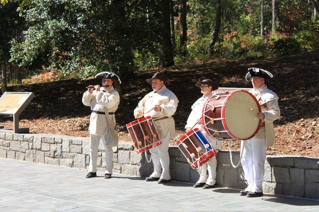 5 musicians in red coats play in front of seated guests.