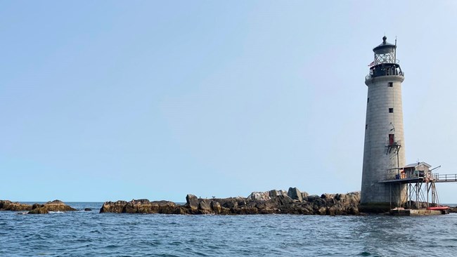 A white lighthouse is surrounded by water with rocks at its base.
