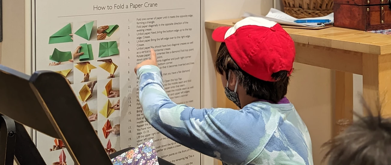 A child wearing a red hat sits on the floor pointing at a poster.