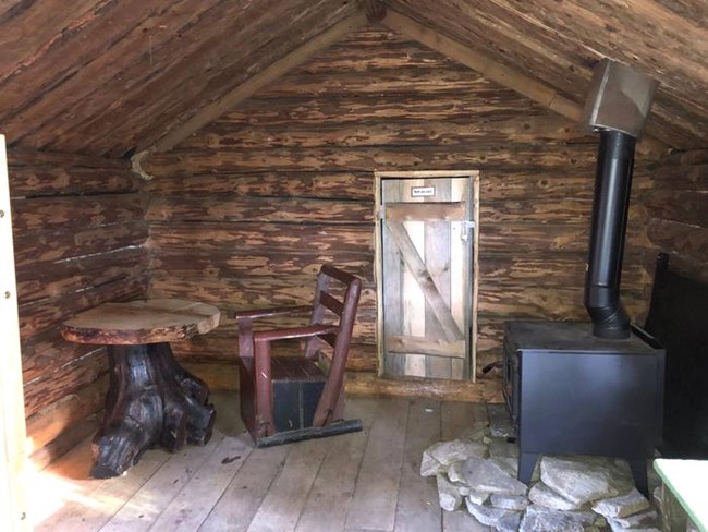 inside a wooden cabin with a wood stove, rustic table and chair