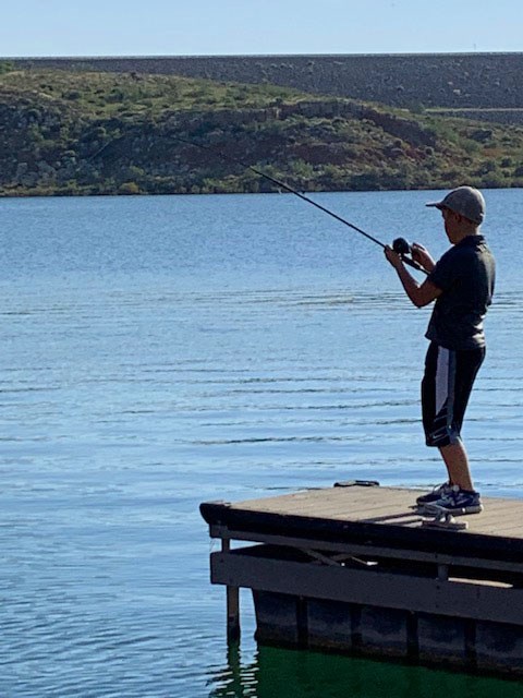 Young fisherman fixing at Sanford Yake at Lake Meredith on a sunny day.  The water and sky are light blue.