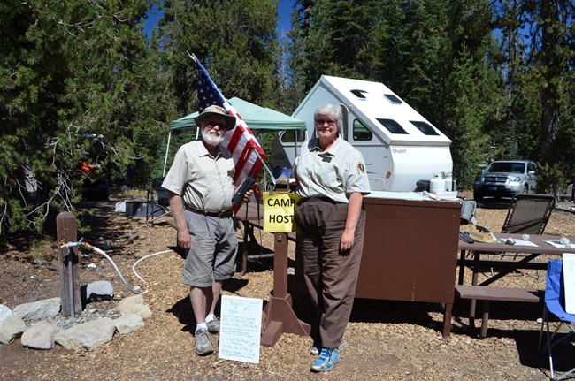 two uniformed camp hosts standing in front of their campsite