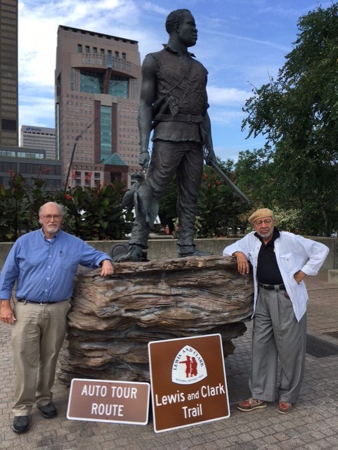 Two men pose with Lewis and Clark Trail Auto Tour Route Signs. Decorative tab reads Partner. Tan background.