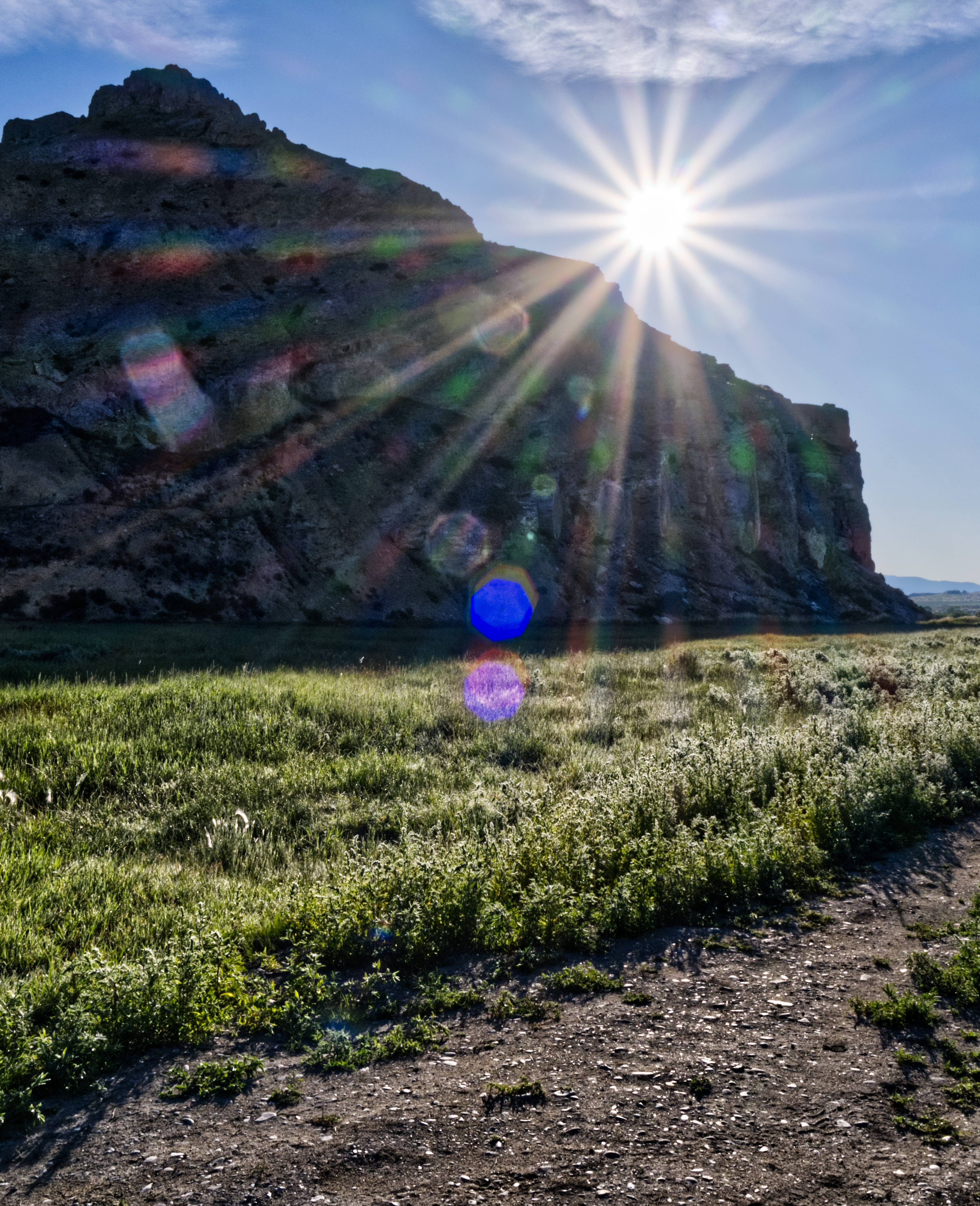 The sun shining over a tall cliff face with a field below