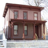 1 story pinkish house with dark red trim and front porch