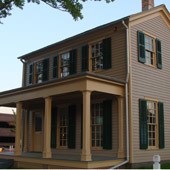 2 story gray-tan house with a porch and green shutters