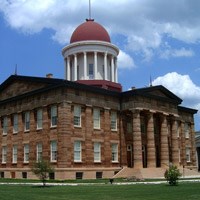 Large brown stone building with columns and steps leading to main door and red dome roof.