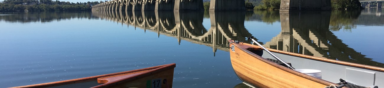 Two canoes docked in the foreground with a bridge extending over water into the distance.