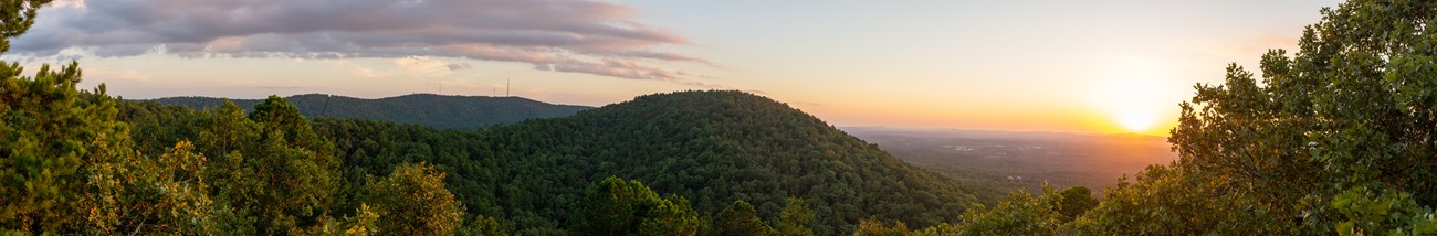 Forested rolling hills and setting sun from a viewpoint on a hill..