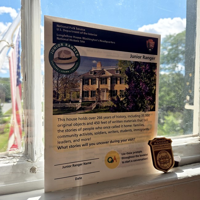 Junior ranger book and wooden badge on white windowsill with American flag in background