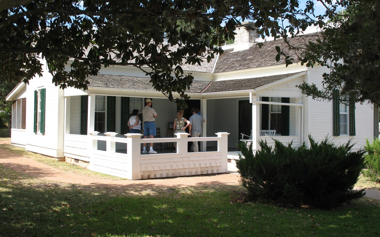 People standing on the front porch of a small, white house.