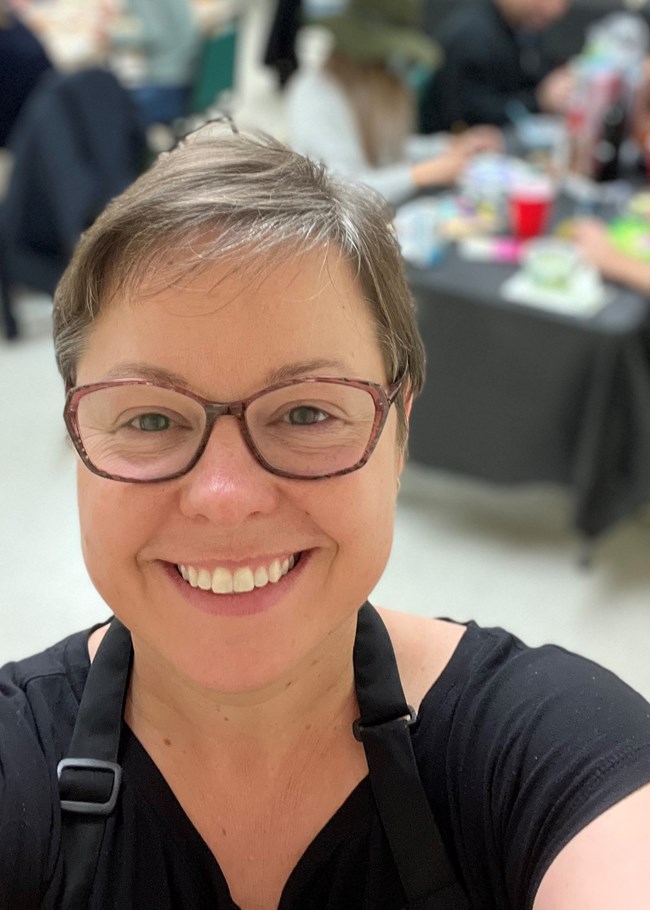 selfie of woman smiling at camera with artists working at tables in background