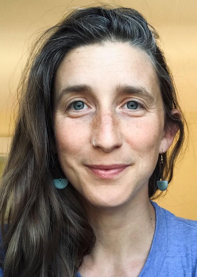 close headshot of woman wearing blue earrings and blue shirt