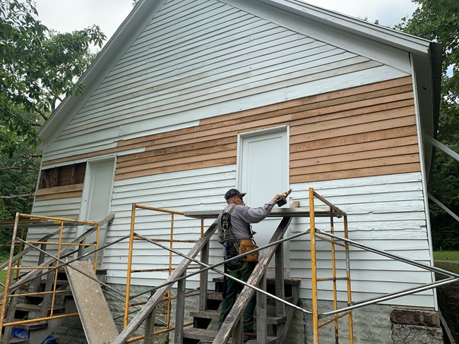 A person standing on scaffolding fixing the wooden siding on a historic building.