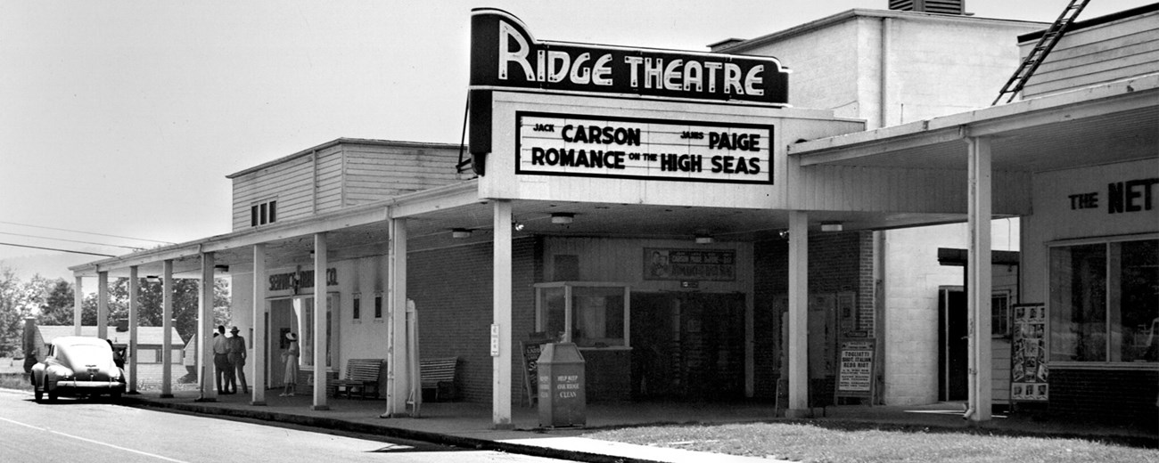 A black and white photo of the Ridge Theatre with a marquee that reads “ Carson Paige, Romance on the High Seas.”