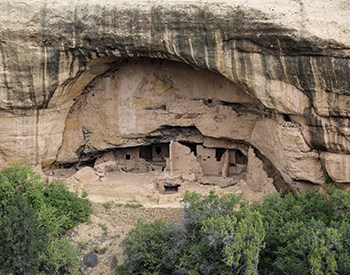 Cliff face with dark brown stains running down its face. Beneath is an ancient, stone-masonry village within an arched alcove.