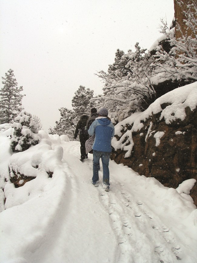 three prople walk up a narrow snow covered slope