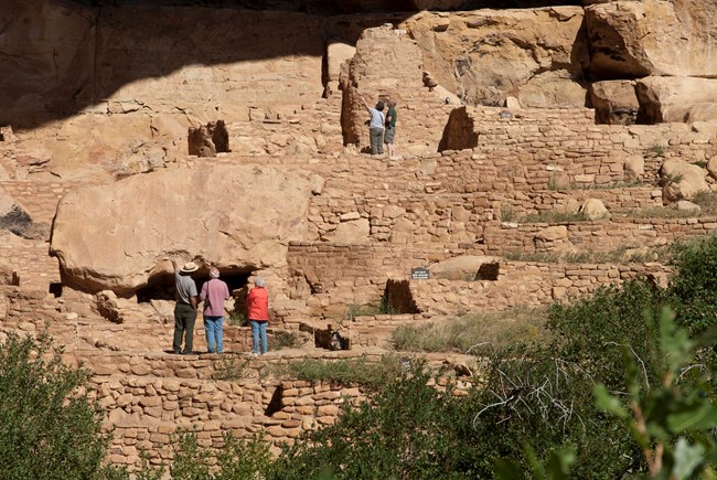 A ranger talks with visitors at a lower tier of step house, while several look on from the upper tiers.
