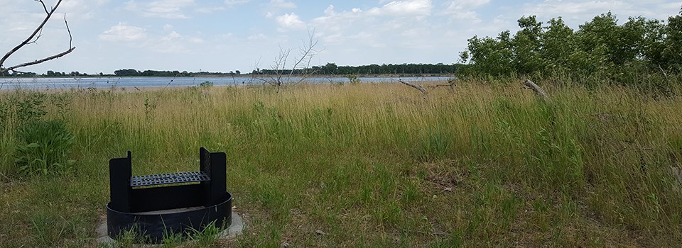 A metal fire ring in a grassy campsite. The Missouri River is in the background.