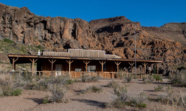 A woodent building with a flag pole sent against a natural rock mountain in sunrise lighting