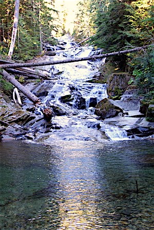 Water falls over a series of polished rock faces into a pool.