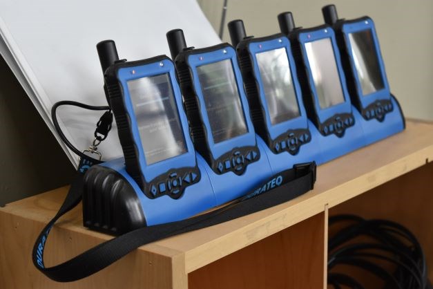 Four black and blue audio description devices in a charging dock.