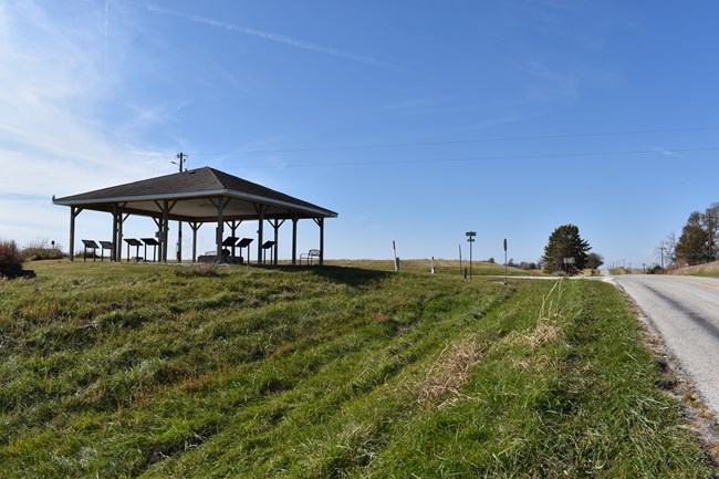 An open-sided kiosk stands just to the left of a paved two-lane road.