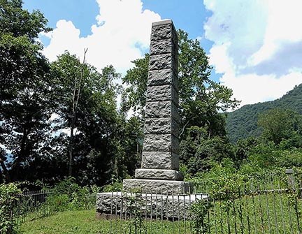 A stone pillar monument surrounded by a fence in a grassy field