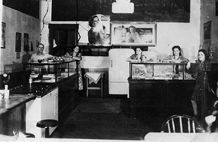 The inside of a restaurant with counters and tables and chairs. Several smiling people lean on the counters.