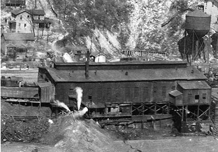 A large rectangular building with railroad tracks coming out of it. Coal hopper rail cars sit on the railroad tracks.