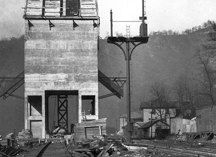 A tall square cement tower on four thick cement legs with metal shoots coming out of it towards railroad tracks