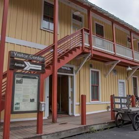 A porch on a yellow building with orange stairs going up to the second floor porch. A sign in front says Visitor Center.