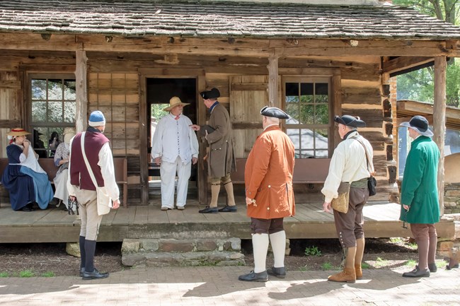Living historians give a presentation on the porch of a log cabin