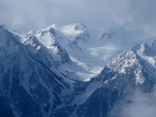 A snow-capped blue mountain among swirling clouds.